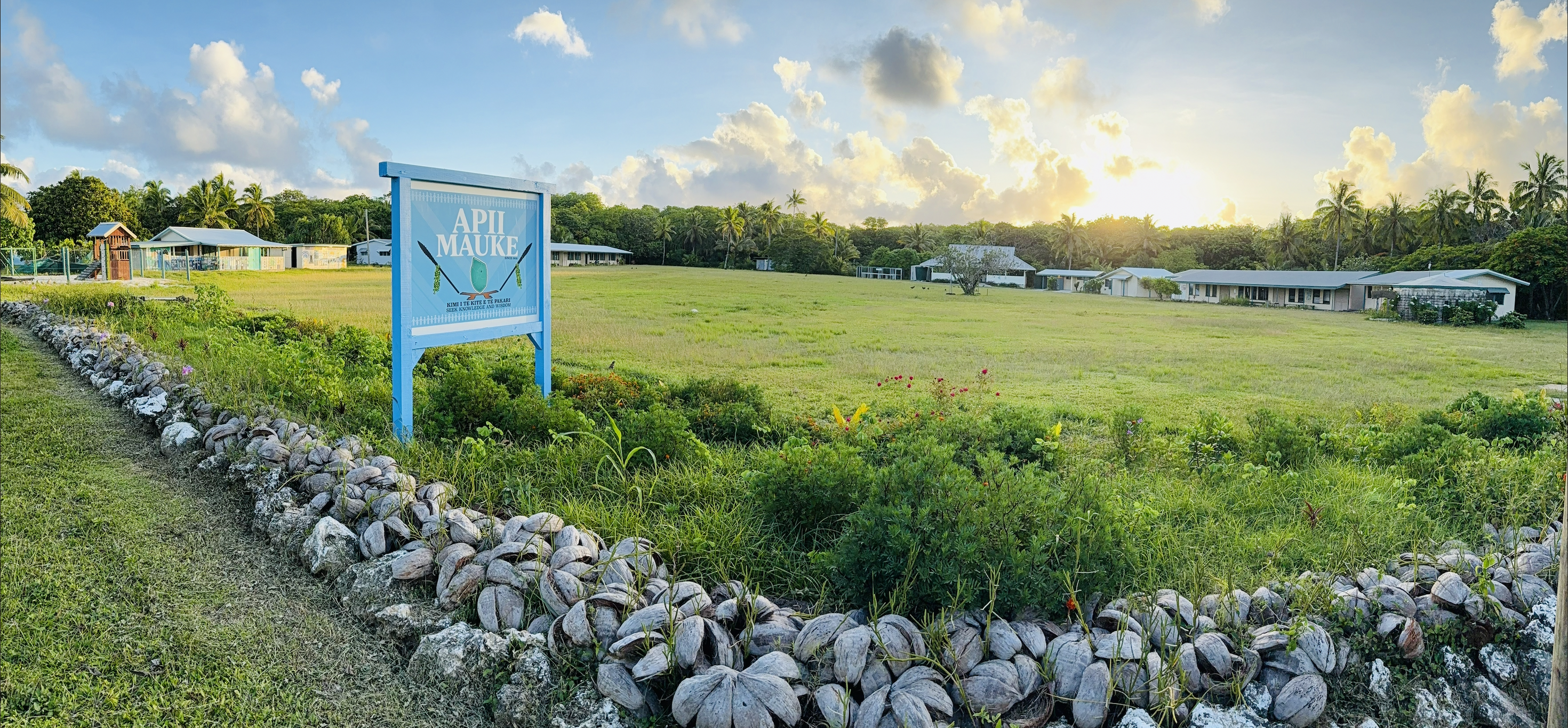 The ʻĀpiʻi Māʻuke school sign standing in
              a field at sunset